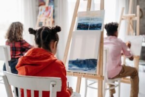 Children engaged in a creative art class, painting on easels indoors.