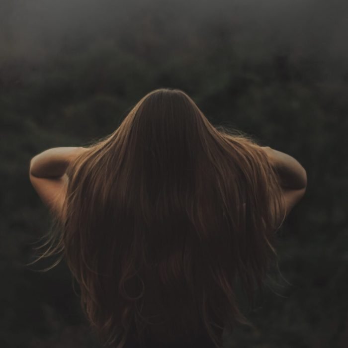 Back view of a woman with long hair, standing in a misty forest.