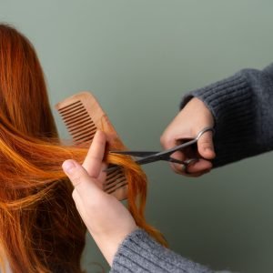 Home Close-up of red hair being trimmed with scissors and comb on green background.