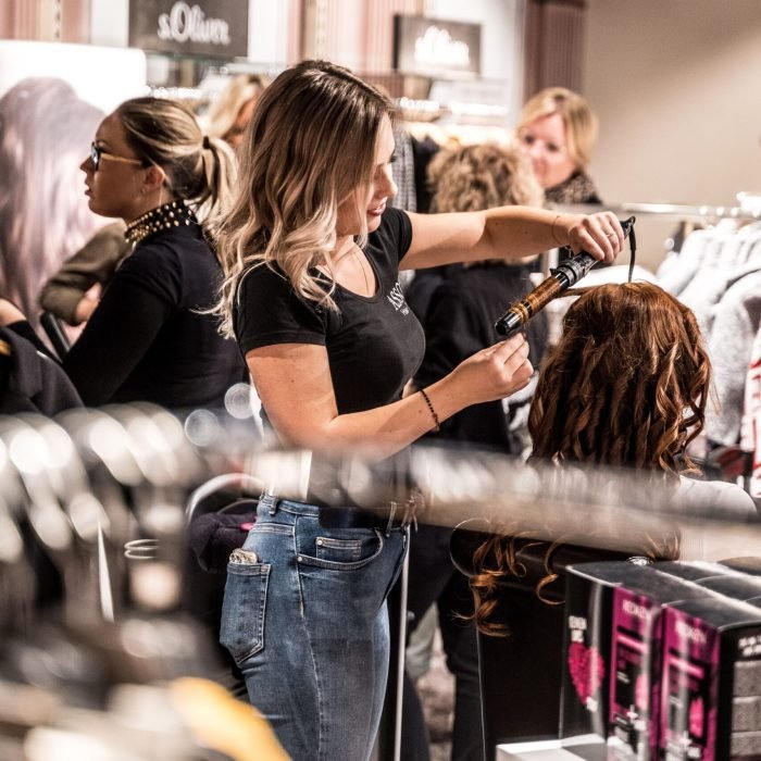 A skilled hairstylist uses a curling iron to style a client's hair in a busy salon.