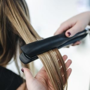 Home Close-up of a hairstylist using a flat iron on blonde hair in a salon setting.
