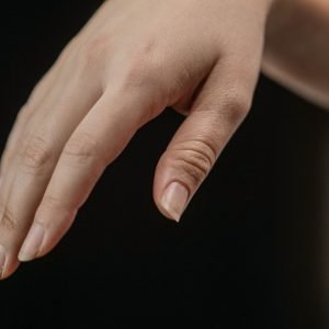 About Us Detailed image of a hand with natural nails, delicately posed against a dark backdrop.