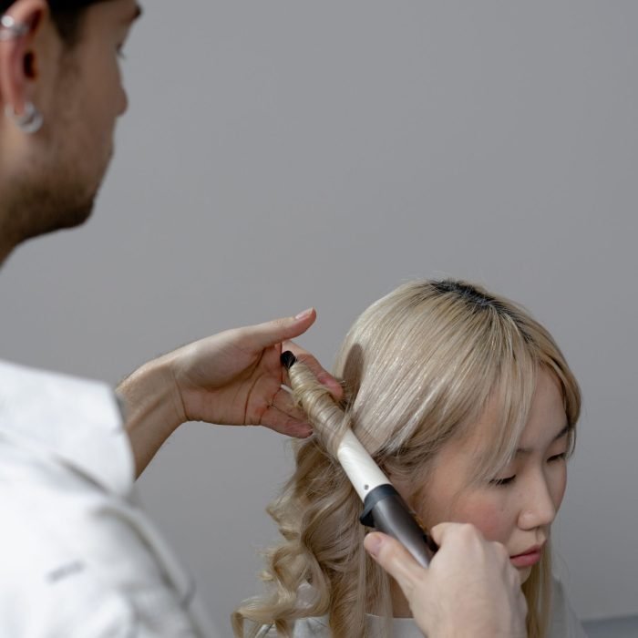 Hairstylist curling a client's hair indoors, showcasing modern hairstyling techniques.