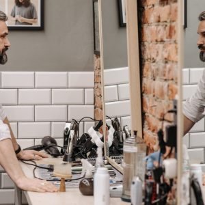 About Us A bearded gentleman examines his reflection in a stylish barbershop setting.