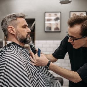 Home A professional barber precisely trimming a client's beard in a modern barbershop.